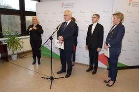 Pokaż zdjęcie: Ludzie stojący, jedna mówi do mikrofonu w obecności mediów